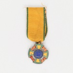 Medalha de Guerra  1942. Executada em prata. Insígnia constituída por cruz de braços iguais esmaltados nas cores verde e amarelo, intercalados por ramos estilizados em esmalte vermelho. Ao centro, medalhão circular esmaltado em azul com inscrição REPÚBLICA DOS ESTADOS UNIDOS DO BRASIL e estrelas em campo central. Reverso com inscrição: MEDALHA DE GUERRA  22-VIII-1942. Suspensa por argola a fita de gorgorão amarela com frisos verdes laterais. Estado conforme fotografias. Medidas: Medalha: Diam.: 1,5 cm. Comp.: 4,5 cm.