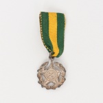 Medalha Militar. Confeccionada em metal prateado. Insígnia constituída por estrela de cinco pontas sobreposta a coroa de louros vazada. Reverso com inscrição: POR DECRETO Nº 2.561 - 29 DE NOVEMBRO DE 1901. Suspensa por argola a fita de gorgorão verde com faixa central amarela. Criada pelo Decreto nº 4.238, de 15 de novembro de 1901, e regulamentada pelo Decreto nº 39.207, de 22 de maio de 1956. A Medalha Militar tem como objetivo recompensar os bons serviços prestados pelos Oficiais e Praças da Marinha, do Exército e da Aeronáutica, em serviço ativo. Medidas: Diam.: 1,5 cm. Comp.: 4 cm.
