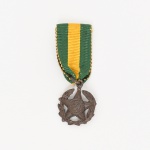 Medalha Militar. Confeccionada em bronze. Insígnia constituída por estrela de cinco pontas sobreposta a coroa de louros vazada. Reverso com inscrição: POR DECRETO Nº 2.561 - 29 DE NOVEMBRO DE 1901. Suspensa por argola a fita de gorgorão verde com faixa central amarela. Criada pelo Decreto nº 4.238, de 15 de novembro de 1901, e regulamentada pelo Decreto nº 39.207, de 22 de maio de 1956. A Medalha Militar tem como objetivo recompensar os bons serviços prestados pelos Oficiais e Praças da Marinha, do Exército e da Aeronáutica, em serviço ativo. Medidas: Diam.: 1,5 cm. Comp.: 4 cm.