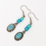 Par de brincos confeccionados em metal prateado, compostos por pendentes ovais com galerias vazadas. Cada pendente apresenta pedra verde em material sintético, inserida em engaste fechado, acima do pendente, duas contas cilíndricas verdes interligadas por argolas metálicas. Sistema de uso por anzol para orelha perfurada. Medida: Comp.: