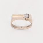 JOIA. PRATA. Anel confeccionado em prata, composto por aro de seção plana, alargando-se na parte superior em mesa retangular. Apresenta pedra incolor de formato quadrado, lapidação facetada, inserida em encaixe rebaixado, com elemento metálico vertical sobreposto atuando como sistema de retenção. Estado conforme fotografias. Medida: Diam.: 2 cm. Peso: 3,8 gramas.