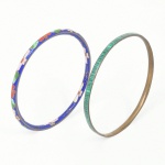 Dois(02) itens: a) Bracelete de formato circular, confeccionado em metal, com decoração em esmaltação cloisonné, fundo em esmalte azul, ornamentado por motivos florais estilizados em esmaltes nas cores verde, branco e vermelho, delimitados por filetes metálicos aparentes. Medida: Diam.: 7,5 cm. b) Bracelete em metal com aplicação em material sintético de tonalidade verde translúcido, apresentando estriações verticais regulares, inserida em canal metálico. Medida: Diam.: 7,3 cm. Estado conforme fotografias.