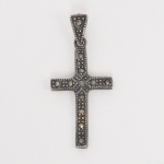 JOIA. PRATA. Pingente em forma de cruz confeccionado em prata com marcasitas, cravadas em sequência ao longo das hastes, com motivo central em arranjo geométrico. Apresenta marca de garantia da prata do toque 0,925 puncionado no verso. Argola de suspensão integrada. Medida total: Alt.: 3.5 x Comp.: 1,7 cm. Peso: 2 gramas.