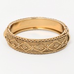 Bracelete rígido de formato circular, confeccionado em metal com acabamento dourado.Corpo composto por faixa central em malha metálica, aplicada sobre estrutura interna, ornamentada por fios torcidos, cordões aplicados e granulação dispostos em padrão geométrico losangular. Bordas com friso em fio torcido e filete perolado. Abertura frontal com sistema de articulação por mola e dobradiça interna. Medida: Diam.: 7 cm.