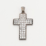 JOIA. PRATA. Pingente confeccionado em prata. Corpo em forma de cruz latina, com superfície frontal inteiramente pavimentada por pedras incolores de lapidação brilhante, cravadas em microgarras. Verso vazado com perfurações circulares correspondentes às cravações. Apresenta marca de garantia da prata do toque 0,925 puncionada no verso e na argola de suspensão. Argola fixa integrada ao passador. Medidas: Alt.: 5,2 x Comp.: 3 cm. Peso: 12 gramas.
