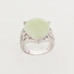 Anel confeccionado em metal prateado, elemento central constituído por quartzo verde, talhado em formato de coração com superfície facetada, fixado por garras, laterais com estrutura vazada em trabalho recortado, formando desenho orgânico. Medida: Diam.: 2 cm.