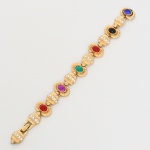 Pulseira confeccionada em metal dourado, composta por módulos articulados. Cada módulo apresenta elemento central com pedra oval cabochão em cores variadas  azul, preta, vermelha, verde e violeta  aplicada em moldura circular, elementos intermediários em formato cilíndrico decorados com fileira de pedras incolores de lapidação redonda facetada, cravadas em canal. Sistema de fecho articulado com lingueta e encaixe. Medida aberta: Comp.: 19 cm.