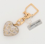 Chaveiro Pierre Cardin confeccionado em metal dourado, composto por mosquetão articulado de formato geométrico, com marcação P. CARDIN gravada na haste interna. Elemento de ligação formado por argolas circulares e elo oval vazado. Pingente em formato de coração, executado em metal com acabamento texturizado, apresentando aplicações em relevo com motivos curvilíneos estilizados, parcialmente guarnecidos por pequenas pedras incolores cravadas em alinhamento. Assinado Pierre Cardin, Paris. Apresenta etiqueta original. Medidas: Alt.: 10 x Comp.: 3,5 cm.