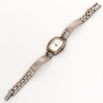 Relógio de pulso feminino da marca GUESS, caixa em metal com acabamento prateado, formato tonneau de perfil curvo. Mostrador branco com numerais arábicos aplicados nos pontos 10, 2, 4 e 8, marcadores geométricos triangulares e trapezoidais nas demais posições, minuteria periférica impressa e ponteiros centrais para horas e minutos. Movimento a quartzo, identificado no verso como Japan Movt. Tampa posterior em aço com gravação circular:  GUESS? INC  GUESS?  JAPAN MOVT. Coroa lateral estriada para ajuste de horário. Bracelete integrado em metal com elos articulados e elementos centrais alongados, placas laterais gravadas GUESS. Fecho dobrável com trava de pressão. Não foi testado. Não está funcionando. Estado conforme fotografias. Medidas: Caixa: Alt.: 2,5 x Comp.: 2 cm. Pulseira: Comp.: 19,5 cm.