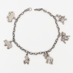 JOIA. PRATA. Pulseira confeccionada em prata, composta por corrente de elos ovais interligados, apresenta pingentes representando figuras diversas, incluindo elefante, suíno, cervídeo, além dos personagens Pato Donald, Mickey Mouse e Pluto, em representação estilizada tridimensional, fixados à corrente por argolas de conexão. Apresenta perda do fecho. Medida: Comp.: 17 cm. Peso: 7,7 gramas.