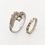 JOIA. PRATA. Dois(02) itens: a) Anel confeccionado em prata, aro de seção plana, apresenta composição frontal formada por dois aros paralelos e curvos, dispostos em sentido levemente diagonal e interligados por estrutura central elevada; aros frontais cravejados com gemas incolores de pequeno calibre, em cravação pavê, com filete lateral microgranulado. Elemento central composto por engaste retangular vazado, com quatro garras, atualmente sem a pedra principal. Apresenta marca de garantia da prata do toque 0,925. Medida: Diam.: 2 cm. Peso: 4,3 gramas. b) Anel confeccionado em prata, aro de seção plana, parte frontal é composta por sequência de módulos retangulares escalonados, intercalados por frisos verticais, tendo ao centro motivo em relevo de formato cruciforme estilizado. Medida: Diam.: 1,5 cm. Peso: 1,4 gramas.