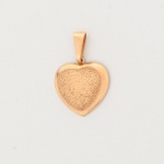 Pingente em formato de coração, confeccionado em metal base com espessurado à ouro; contorno abaulado e superfície frontal texturizada por gravação irregular, verso liso, polido, com leve rebaixo central acompanhando o contorno interno. Argola fixa articulada a contra-argola, com passador superior em forma trapezoidal, integrado ao conjunto. Medidas: Alt.: 2,5 x Comp.: 2 cm.