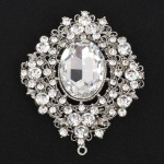 Broche/pendente de formato ovalado, confeccionado em metal com acabamento prateado, apresentando dupla função; centro composto por pedra oval facetada, incolor, lapidação mista com mesa ampla e facetas geométricas regulares, fixada por garras, contorno estruturado em desenho vazado com volutas e elementos fitomórficos, guarnecido por múltiplas pedras incolores de lapidação brilhante, de diferentes diâmetros, igualmente cravadas por garras.Parte superior provida de argola fixa para uso como pendente. Verso com fecho tipo alfinete, sistema articulado com trava de segurança. Estado conforme fotografias. Med.: Alt.: 7 x Comp.: 6 cm.