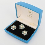 BIJUTERIA. Conjunto Rodiprat, composto por anel e par de brincos em metal prateado com pérola sintética e gemas verdes, acondicionado em estojo original identificado Rodiprat, apresentam composição floral estilizada em montagem elevada, cada uma com pérola central esférica de tonalidade creme, fixada por engaste em colarinho, circundada por pedras incolores lapidadas em brilhante, cravadas por garras, intercaladas por gemas verdes em lapidação navete (marquise) igualmente cravadas por garras/ armação vazada com galerias abertas, permitindo passagem de luz às pedras, anel apresenta aro liso e cabeça elevada em estrutura tipo cúpula, brincos com sistema de fecho tipo pressão (clip). Medidas: Brincos: Diam.: 2 cm; Anel: Alt.: 3 x Diam.: 2 cm.