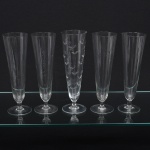 Conjunto de tulipas em meio cristal, translúcido e incolor, bojo longo de formato obcônico, fuste curto e cilíndrico, base circular. Composto de cinco(05) unidades. Medidas: Alt.: 23 x Diam.: 7 cm.