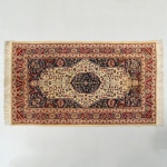 Tapete Kashimir, fomato retangular de composição axial, apresentando medalhão central circular lobado sobre campo marfim com decoração floral estilizada. Quartos de medalhão nas extremidades do eixo longitudinal. Campo secundário em tonalidade azul-escuro com arabescos e elementos fitomórficos. Bordadura principal vermelha decorada por sequência de motivos florais repetitivos, acompanhada por guardas internas múltiplas. Estado conforme fotografias. Medidas: Alt.: 173 x Comp.: 94 cm.