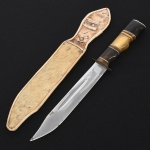 Faca de coleção com lâmina em aço inox, gravada "Caroca - Inox - Campina Grande". Lâmina de perfil clip Point, apresentando canal longitudinal junto ao dorso. Guarda metálica simples, empunhadura anatômica composto por segmentos torneados em chifre bovino de diferentes tonalidades, intercalados por anéis metálicos, terminando em pomo metálico. Produção brasileira, Campina Grande(PB), típica da cutelaria nordestina destinada ao uso de caça e campo. Acompanha bainha em couro, estruturada e revestida externamente por pelo(provavelmente bovino), no estado, conforme fotografias. Medida da faca: Comp.: 23 cm.