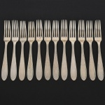 RADIO ALPACA. Conjunto de garfos grandes confeccionadas em alpaca espessurado à prata, cabo de ponta oval, ricamente relevado com folhas de acanto e borda contornada por fileira perlada. Marca da manufatura puncionada no verso. Composto de doze(12) unidades. Apresentam marcas de uso e do tempo, vide foto. Medida: Comp.: 19,5 cm.