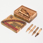 Pena metálica para escrita  D. Leonardt & Co., Inglaterra. Pena metálica para caneta de pena (dip pen), em aço com revestimento dourado, corpo estampado com reservatório integrado e fenda longitudinal para condução e controle do fluxo de tinta. Apresenta ponta conformada de perfil cônico com abertura central. No talão cilíndrico constam inscrições estampadas: D. Leonardt & Co., HEMISPHERICAL POINT e ENGLAND, indicando fabricação pela tradicional indústria inglesa de penas metálicas estabelecida em Birmingham, importante centro de produção de instrumentos de escrita entre os séculos XIX e XX, modelo corresponde ao tipo de ponta hemisférica, concebido para proporcionar traço uniforme e maior resistência ao desgaste durante a escrita contínua. Peça integrante da produção industrial inglesa de penas de aço destinadas à escrita manual com tinta líquida. Apresentam sinais de oxidação, visíveis nas fotografias. Acondicionadas em caixa Estojo original em cartonagem litografada, com decoração policroma e inscrição D. Leonardt & Co.s, contendo referência ao modelo Eureka  Hemispherical Pointed Pens. A tampa apresenta emblema heráldico e menção honorífica To H.M. The King of Italy, além de composição gráfica com medalhões alusivos às distinções obtidas pela manufatura. A lateral do estojo traz relação de premiações industriais internacionais atribuídas à fábrica, incluindo medalhas obtidas em exposições universais e industriais, entre elas Moscou (1872), Viena (1873), Paris (1878), Sydney (1880) e Melbourne (1881), além de Adelaide (1887); verso apresenta texto explicativo em língua portuguesa informando a autenticidade da marca e identificando a empresa D. Leonardt & Cia., Birmingham, fabricante de penas metálicas com ponta hemisférica, tecnologia destinada a proporcionar maior regularidade no fluxo de tinta e durabilidade da ponta. Aproximadamente vinte e oito(28) unidades. Medida: Comp.: 4,2 cm.