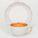 Porcellana Mauá, Mauá - SP(Fundada em 1937 por Fritz Erwin Schmidt / ativa até 1968). Xícara para café da década de 1950/60 em porcelana esmaltada, bojo hemisférico e pires circular de aba levemente ondulada, decoração minimalista, com filetes dourados nas bordas da xícara e do pires, enquanto o interior da xícara apresenta douração integral (gilding), criando contraste com o exterior em esmalte azul claro, asa lateral em voluta parcialmente recoberta por douração, pires acompanha a mesma linguagem decorativa, apresentando duplo filete dourado delimitando o centro e a borda. Marca da manufatura na base em verde: PORCELLANA MAUÁ. Medidas: Xícara: Alt.: 4 x Comp.: 8 x Larg.: 6,5 cm; Pires: Diam.: 10,5 cm. Apresenta manchas do tempo na superfície externa da xícara.