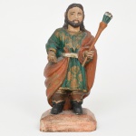 ARTE SACRA. São Judas Tadeu. Imagem Sacra executada em madeira entalhada e policromada, figurada de pé sobre base prismática. Apresenta-se de pé, com cabelos longos e barba, trajando túnica longa verde com decoração dourada e manto vermelho, cingido por faixa à cintura, segura na mão direita bastão ou clava, atributo iconográfico associado ao apóstolo, instrumento ligado ao seu martírio segundo a tradição hagiográfica, policromia apresenta tratamento cromático em verde e vermelho com ornatos dourados, com modelação simplificada das pregas do vestuário e tratamento frontal da figura. Calça botas negras e apoia-se sobre base retangular de madeira policromada. Medidas: Alt.: 15,5 x Comp.: 7 x Larg.: 5,5 cm.