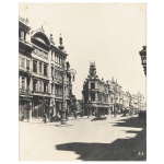 Fotografia em preto e branco aplicada sobre moldura de madeira, impressão sobre papel, representando vista da Avenida Central (atual Avenida Rio Branco), com edificações de caráter eclético alinhadas ao longo da via, destacando fachadas ornamentadas, torreões e elementos decorativos de influência europeia. Presença de postes de iluminação pública em ferro fundido, circulação de pedestres e veículo automotor de época. Medidas: Alt.: 39 x Comp.: 29,5 cm.