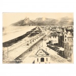 Fotografia em preto e branco, impressão sobre papel aplicada sobre moldura de madeira, representando a orla de Ipanema e Leblon, no Rio de Janeiro, com vista panorâmica da faixa litorânea, avenida marginal e alinhamento de postes de iluminação ao longo da via. Em primeiro plano, edificações residenciais e estruturas urbanas, e ao fundo o Morro Dois Irmãos. Inscrição manuscrita no canto inferior indicando Vieira Souto, Ipanema  1929. Atribuída ao fotógrafo Augusto Malta. Medidas: Alt.: 29 x Comp.: 39 cm.