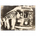 Fotografia em preto e branco aplicada sobre moldura de madeira, impressão sobre papel, representando bonde urbano identificado TIJUCA, com passageiros embarcados e grupo de transeuntes ao redor, veículo nº 2050, em via pública. Medidas: Alt.: 29 x Comp.: 39 cm.