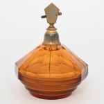 Frasco de perfume para toucador do início do século XX, c1920/30, período Art Déco, executado em meio cristal prensado, translúcido, tonalidade âmbar, ricamente facetado com dez lados, base escalonada decrescente, montagem superior em metal com anel estriado e bico pulverizador lateral, dotado de mecanismo interno de sucção constituído por tubo capilar(não testado), sistema originalmente acionado por pera compressível de borracha, atualmente ausente. Apresenta bicado no fundo da base. Medidas: Alt.: 14 x Diam.: 11 cm.