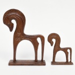 Duas(02) esculturas executadas em metal fundido, representando figuras estilizadas de equinos, estilo etrusco ou grego antigo, de perfil, com corpo vazado e estrutura linear, apoiadas sobre base retangular integrada. Superfície com pátina homogênea em tonalidade ferruginosa, com elementos decorativos incisos e pontilhados na região da cabeça e do tronco. Medidas: Alt.: x Comp.: x Larg.: