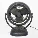 Ventilador elétrico de mesa, com estrutura em metal, composto por base semicircular, suporte articulado em arco e corpo circular com grade frontal em arame e hélice tripla metálica. Motor elétrico interno, com acionamento por chave frontal deslizante. Placa de identificação inferior indicando fabricante WAWM, com especificação Circulador de Ar, modelo 10, tensão 110/220 V. Não está funcionando. Fio está partido, necessita refazer parte elétrica. Estado de conservação conforme fotografias. Medidas: Alt.: x Diam.: