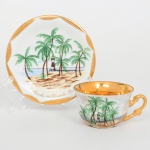 Porcellana Mauá, Mauá - SP(Fundada em 1937 por Fritz Erwin Schmidt / ativa até 1968). Xícara para café  porcelana nacional, esmaltação branca, decoração manual em policromia representando paisagem tropical com coqueiros e o Farol de Itapuã, na cidade de Salvador, Bahia; composição apresenta faixa litorânea com areia, mar ao fundo e o farol característico em vermelho e branco, acompanhado por filetes paisagísticos e aves estilizadas. A xícara apresenta bojo hemisférico com interior totalmente dourado, apoiado sobre base circular, e alça lateral em voluta estilizada inteiramente dourada. A decoração externa repete o motivo paisagístico com coqueiros inclinados e vista parcial do farol. O pires possui borda facetada com larga faixa dourada, contendo no centro a mesma representação do Farol de Itapuã, acompanhada de inscrição manuscrita em douração: Farol de Itapoã  Bahia. Marca da manufatura no verso sob marca de sobreposição. Medidas: Xícara: Alt.: 4 x Comp.: 8,5 x Larg.: 6,5 cm; Pires: Diam.: 10,5 cm. Apresenta marcas de uso, vide fotos.