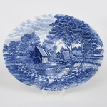 Johnson Brothers, Staffordshire - Inglaterra(Fundada em 1883). Belíssima travessa oval executada em faiança inglesa, padrão Watermill. Decoração monocromática em azul sob esmalte, representando paisagem rural com moinho hidráulico, executada por estampagem. A composição mostra edifício de moinho com roda dágua em funcionamento, pequeno dique e queda dágua, acompanhados por casas campestres, árvores frondosas, figuras humanas em ambiente bucólico e céu anuviado ao fundo; orla modelada com delicado movimento ondulado, borda recortada com arcos em repetição. Marca da manufatura no verso. Medida: Comp.: 35 x Larg.: 27 cm.