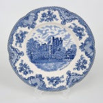 Johnson Brothers, Staffordshire - Inglaterra(Fundada em 1883). Prato de coleção em faiança inglesa da década de 1930/40. Série "The Old Britain Castle". Esmaltagem de tom marfim, dotada de profusa decoração em estampagem de tonalidade azul; este exemplar apresenta, ao centro, imagem do Castelo de Blarney(Blarney Castle) no ano de 1792, em paisagem lacustre contendo personagens, árvores e céu coberto por nuvens; orla modelada com ligeiro movimento ondulatório, ricamente ornamentada com flores e elementos fitomorfos, borda recortada em arcos e contornada por barrado contínuo de padrão geométrico. Marca da manufatura no verso. Med.: Diam. 25,5 cm. (O Castelo de Blarney é uma fortificação medieval localizada em Blarney, a oito quilômetros da cidade de Cork, no condado de mesmo nome, na República da Irlanda).