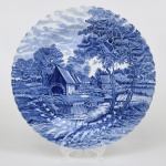 Johnson Brothers, Staffordshire - Inglaterra(Fundada em 1883). Grande prato de coleção executado em faiança inglesa, padrão Watermill. Decoração monocromática em azul sob esmalte, representando paisagem rural com moinho hidráulico, executada por estampagem. A composição mostra edifício de moinho com roda dágua em funcionamento, pequeno dique e queda dágua, acompanhados por casas campestres, árvores frondosas, figuras humanas em ambiente bucólico e céu anuviado ao fundo; orla modelada com delicado movimento ondulado, borda recortada com arcos em repetição. Marca da manufatura no verso. Medida: Diam.: 31 cm.