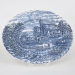 Wood & Sons, Burslem - Inglaterra(Fundada em 1865). Excepcional travessa oval executada em faiança inglesa, decorada com estampagem em monocromia azul, série 'The Post House'. A cena central representa uma diligência puxada por quatro cavalos em frente a uma estalagem rural de arquitetura tradicional, onde se reúnem viajantes e personagens em diferentes atividades, identificada por placa com a inscrição Red Lion. Em segundo plano, observam-se árvores frondosas, construções de apoio, e céu anuviado ao fundo compondo paisagem campestre; borda suavemente recortada e moldada em delicado movimento ondulado, acompanhando o enquadramento da decoração. Marca da manufatura no verso. Med.: Comp. 35 x Larg. 27,5 cm.