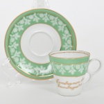 Porcelana Real, Mauá - SP(Fundada em 1943 por Fritz Erwin Schmidt). Xícara de coleção em porcelana nacional, esmlatação branca, com aba e bojo decorados por faixa em verde com motivo repetitivo de ramagem estilizada em reserva branca, delimitada por filetes em douração. Pires de formato circular com cavidade central para encaixe da xícara. Xícara de formato obcônico com alça lateral estilizada. Inscrição aplicada em douração na xícara: Lembrança de Caruaru. Marca da manufatura no verso. Medidas: Alt.: 6 x Comp.: 7,5 x Larg.: 6  cm. PIres: Diam.: 11 cm.