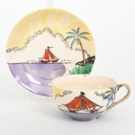 Xícara para chá em faiança japonesa, bojo hemisférico com asa lateral em arco, com acabamento anacarado. Decoração manual em esmaltes sobre vidrado, com composição paisagística estilizada: embarcação à vela de pano vermelho sobre faixa dágua em tom violáceo, acompanhada por palmeira inclinada e  vegetação, sob céu em gradação amarelada com nuvens delineadas. Verso com marca de manufatura em esmalte vermelho e inscrição Marca Registrada  Made in Japan. Apresenta desgaste no filete metálico da asa, craquelê no vidrado e pequenas marcas de uso, visíveis nas fotografias. Medidas: Xícara: Alt.: 5 x Comp.: 10,5 x Larg.: 8,5 cm; Pires: Diam.: 13 cm.