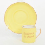 Porcelana Schmidt - Brasil(Fundada em 1945). Xícara de coleção, para café, em porcelana nacional, esmaltação externa integralmente de tonalidade amarelo, internamente na cor branca, bojo cilíndrico contendo inscrição "Lembrança de Araxá" aplicada em douradura, alça lateral em voluta, pires de borda recortada em ondulações, bordas e contornos arrematados com filete dourado. Marca da manufatura no verso. Medidas: Xícara: Alt.: 4,5 x Comp.: 6 cx Larg.: 4 cm; Pires: Diam.: 10 cm.