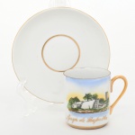 Xícara para café em porcelana esmaltada, manufatura Waka Mizu - Brasil, bojo cilíndrico com alça aplicada, bordas e filetes em ouro; decoração com cena paisagística intitulada Igreja de Pampulha e inscrição Lembrança de Belo Horizonte; pires circular com cavidade central e filete dourado. Verso com marca da manufatura. Medidas: