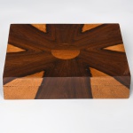 Caixa em madeira nobre com tampa removível, composta por painéis de lâminas dispostas em marchetaria radial formando desenho geométrico em contraste de tonalidades. Tampa de formato retangular, superfície superior com composição em raio de sol, obtida por disposição de veios naturais da madeira em segmentos triangulares convergentes para campo central circular; laterais com continuidade do desenho em lâminas contrastantes. Medidas: Alt.: x Comp.: x Larg.: