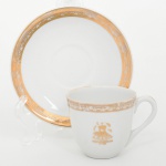 Porcelana Rio Branco/Cia. Brasileira de Vidros, Rio de Janeiro - RJ(Fundada em 1947, ativa até 1967). Elegante xícara de coleção em porcelana, esmaltação na cor branca, decoração executada em douração, composta por faixa ornamental contínua junto à borda da xícara e do pires, formada por friso com padrão arquitetônico estilizado, na face frontal da xícara apresenta emblema dourado representando a Catedral Metropolitana de Brasília, com inscrição Brasília  Obra do Século XX e datas 19591960, em referência à construção da catedral projetada por Oscar Niemeyer. Tipologia de peça comemorativa / souvenir institucional alusiva à construção de Catedral Metropolitana de Brasília. Marca da manufatura no verso. Medidas: Xícara: Alt.: 5 x Comp.: 7,5 x Larg.: 6 cm. Pires: Diam.: 11 cm.