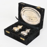 Conjunto composto por saleiro, pimenteiro e bandeja oval, executado em metal prateado, apresentam corpo bojudo apoiado sobre três pés curvos, com tampas perfuradas e bordas ornamentadas, bandeja possui decoração gravada e borda trabalhada, formando conjunto de mesa destinado ao serviço de condimentos. Acondicionado em estojo original revestido, com interior em veludo moldado para acomodação das peças. No verso observa-se etiqueta da Internazionale Silver Co., indicando produção industrial de metal prateado para uso doméstico. Medidas: