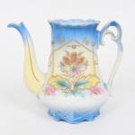 Belíssimo bule para café em porcelana(sem tampa), provavelmente europeu do início do século XX, período  estilo Art Nouveau,  corpo aproximadamente cônico com base recortada em gomos, colo levemente estreitado e bordo ondulado. Bico vertedor alongado, de perfil curvo ascendente, com sulco central e filete dourado; asa posterior vazada, de desenho sinuoso, com terminação em volutas. Decoração em esmalte policromo com aplicação de douramento em relevo. Fundo com gradiente em tons de azul, amarelo e rosa. No anverso, reserva central com motivo floral estilizado, composta por flor de quatro pétalas com tratamento pontilhado em ouro, ladeada por folhagem simétrica. Enquadramento por elementos geométricos e festonados, com pequenas aplicações em relevo dourado simulando contas e pingentes. Bordo superior e detalhes do bico e da asa realçados por filetes dourados. Apresenta perda da tampa. Medidas: Alt.: 19,5 x Comp.: 23 x Larg.: 13 cm.