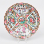 Prato fundo em porcelana chinesa, decoração policromada no estilo famille-rose. Decoração policromada esmaltada sobre o vidrado, em paleta predominante de rosa, verde, amarelo, azul e vermelho, com contornos em traço escuro e filete de tom "rouge de fer" no bordo; ornamentação apresenta composição radial dividida em reservas, alternando painéis florais e frutíferos estilizados com cenas figurativas chinesas representando personagens em ambiente doméstico ou palaciano. As reservas são delimitadas por faixas com padrão geométrico inspirado em meandro grego, intercaladas com motivos vegetais e elementos ornamentais estilizados; centro com medalhão circular com arranjo floral e frutífero, enquanto a aba é ricamente preenchida por motivos florais, frutos e elementos decorativos sinuosos, característicos das porcelanas chinesas produzidas para exportação e inspiradas no repertório decorativo famille-rose. Verso marcado com selo vermelho e caracteres chineses. Medida: Diam.: 23 cm.