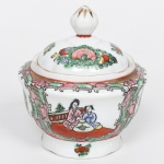 Açucareiro em porcelana chinesa, esmaltação branca, dotada de decoração policromada no estilo famille-rose,  tampa abaulada com pomo em forma de botão. Apresenta decoração policromada esmaltada sobre o vidrado, em paleta predominante de rosa, verde, vermelho, amarelo e azul, com realces em contorno escuro e filetes dourados aplicados nos bordos e no bico, ornamentação segue repertório inspirado no estilo famille-rose, caracterizado por painéis em reservas cartuchadas delimitadas por volutas e elementos fitomorfos, bojo apresenta cena figurativa com personagens chineses em ambiente doméstico ou palaciano, enquanto outros painéis exibem arranjos florais e frutíferos estilizados, organizados em composição simétrica, faixa superior preenchida por arabescos vegetais densamente distribuídos, típica solução ornamental em porcelanas chinesas decoradas para exportação. Verso com marca em selo vermelho com caracteres chineses, indicando fabricação na China. Medidas: Alt.: 12,5 x Diam.: 11,5 cm.