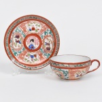 Xícara para chá executada em porcelana japonesa, dita "casca de ovo", estilo imari; bojo hemisférico, alça latral em voluta, internamente com esmaltação branca, externamente decorado com esmaltes policromos predominantemente em vermelho-ferro, verde e azul, com detalhes em dourado, ornamentação apresenta composição radial em reservas, delimitadas por contornos em vermelho e preenchidas com cenas figurativas e motivos ornamentais, medalhão central do pires figura personagem feminina em trajes tradicionais japoneses, rodeada por ramos florais estilizados. Ao redor distribuem-se cartelas alternadas com cenas narrativas, paisagens arquitetônicas e personagens, além de elementos decorativos como nuvens estilizadas e dragões delineados em vermelho, bordas contornadas por faixa com folhagens na tonalidade verde em verde. Verso contendo marca impressa em vermelho MADE IN JAPAN, indicando produção destinada a exportação. Medidas: Xícara: Alt.: 5 x Comp.: 12,5 x Larg.: 10 cm. Pires: Diam.: 14 cm.