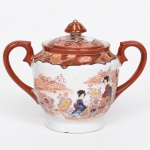Açucareiro executada em porcelana japonesa, esmaltação branca, decorada em esmaltes policromos no estilo Imari; corpo globular assente sobre base circular, provido de duas alças laterais em voluta, ambas integralmente revestidas por esmalte vermelho-ferro, tampa encimada por botão em forma de cúpula decorado com filetes dourados; decoração em esmaltes policromos sobre o vidrado, predominando o vermelho-ferro, complementado por azul, amarelo e douração, bojo apresenta cenas figurativas com personagens femininas em trajes tradicionais japoneses, representadas em meio a paisagem estilizada com construções, vegetação e composição floral abundante, disposta em friso contínuo ao redor do corpo, parte superior do bojo e da tampa é ornamentada por faixa recortada com reservas geométricas e florais, com contornos realçados em preto e detalhes em dourado. Fundo com marca impressa em vermelho MADE IN JAPAN, indicando produção destinada ao mercado de exportação. Medidas: Alt.: 12 x Comp.: 16 x Larg.: 9,5 cm. Tampa apresenta acentuada rachadura colada, demanda restauro.