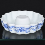 Porcelana Real, Mauá - SP(Fundada em 1943 por Fritz Erwin Schmidt). Forma refratária em porcelana nacional, esmaltação branca, formato circular moldada com borda ondulada (recortada) e tubo central, destinada à preparação de bolos ou pudins, decoração apresenta bordadura floral estilizada em azul, composta por pequenos ramos, flores e folhagens distribuídos ao longo da parede externa, executados em tonalidade azul sob o vidrado. Verso com marca da manufatura, acompanhada das inscrições Real  Made in Brazil  Calorama, acompanhada da inscrição Legítima Porcelana Super Refratária para Forno e Mesa, indicando peça destinada ao uso culinário direto em forno. Consta ainda a indicação Genuine Porcelain Oven Ware  Cap. 38 oz  Lead Free Glaze, informando capacidade aproximada e vidrado livre de chumbo. Medidas: Alt.: 5,5 x Diam.: 21,5 cm.