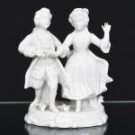 VIEIRA DE CASTRO (Rio de Janeiro, ativa aproximadamente entre 1939 e 1979). Grupo escultórico executado em porcelana nacional, esmaltação vítrea de tonalidade branca, representando casal, trajando vestimenta de época, em cena galanteio, base oblonga relevada com conchas e volutas circundando a borda, detalhes relevados na própria pasta. Marca da manufatura no verso. Apresenta quebradura colada na saia. Medidas: Alt.: 18,5 x Comp.: 14,5 x Larg.: 10 cm.